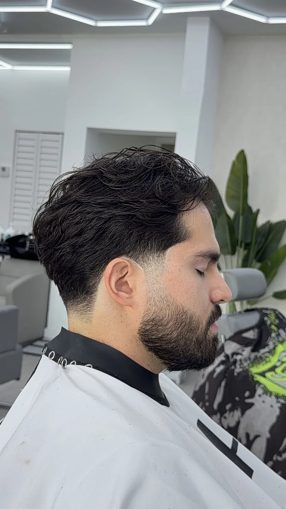 A wavy, textured haircut with tapered sides and a shaped beard